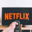 closeup photo of person holding panasonic remote control in front of turned on smart television