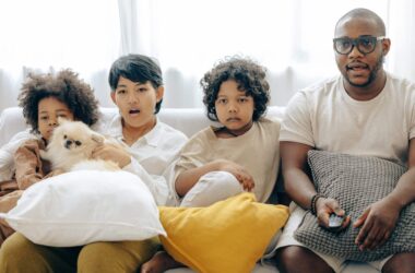 interested multiracial family watching tv on sofa together with dog