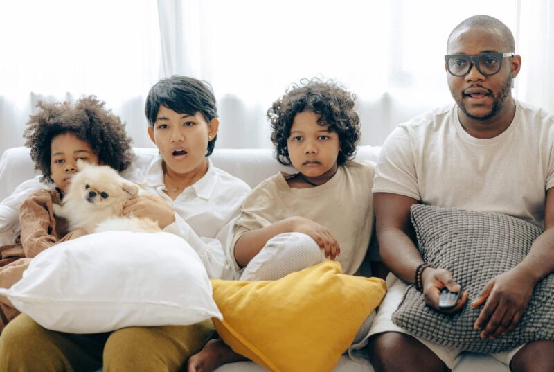 interested multiracial family watching tv on sofa together with dog